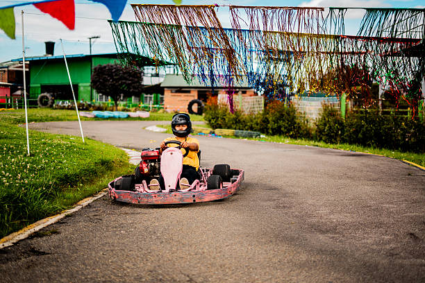 A single go-kart driver navigates a winding outdoor track, surrounded by vibrant decorative streamers and a green landscape. The scene captures the excitement of recreational karting in a playful, festive environment.