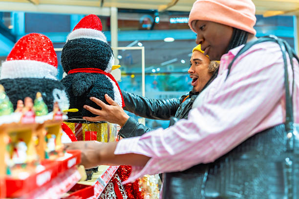 Happy young adults browsing and selecting christmas decoration items, a man excitedly interacting with a large penguin display figure in a festive store