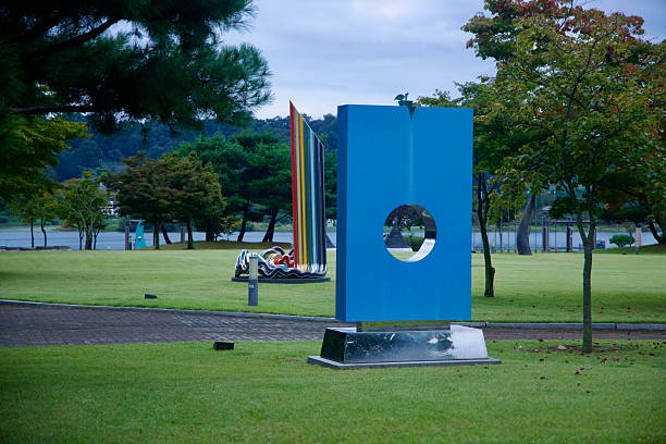 Contemporary outdoor sculptures dot the lawn at Jungangtap Park beside the South Han River, including a blue geometric piece with a circular cutout and multicolored forms beyond.