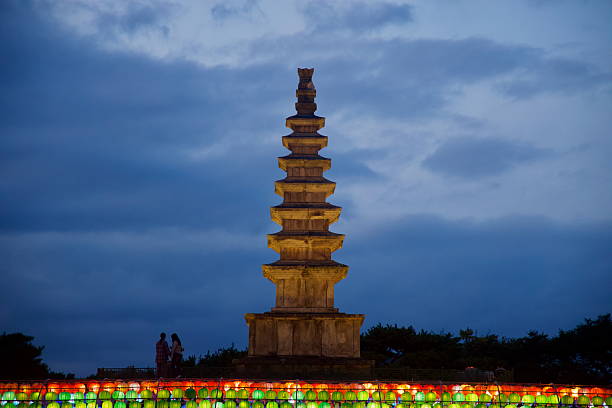The stone sevenstory Central Tower stands beyond bright rows of lanterns at Jungangtap Park, silhouetted figures pausing on the platform as evening.