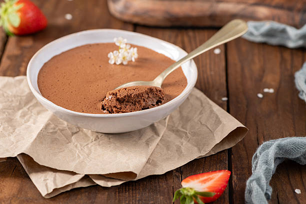 istock Rich and airy chocolate mousse in a white bowl, a golden spoon lifting a portion, garnished with delicate white flowers, resting on crumpled parchment paper and a wooden table 2247542253