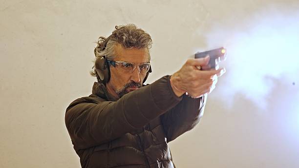 Male shooter shoots handgun at target inside shooting range. Mature man learning self devense and target sports. Training sports.