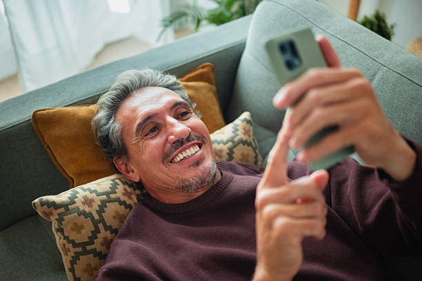 istock Mid adult man relaxing on sofa using smartphone 2247543115