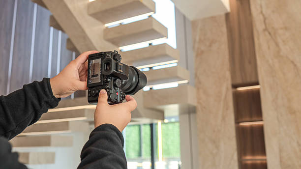 istock Photographer holding a camera, capturing a modern interior with a staircase 2247549343
