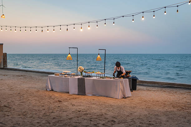 Chef arranging fresh food at a beachside catering buffet with ocean backdrop.