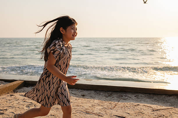 Smiling girl is running freely along the ocean shoreline during sunset.