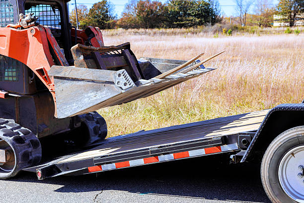 istock Loader skid steer equipment unloading materials from transport trailer on construction site 2247561417