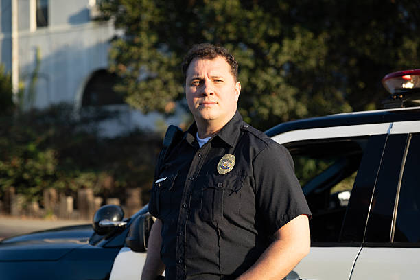 istock White Policeman Looks Off-camera in Front of His Squad Car 2247565633