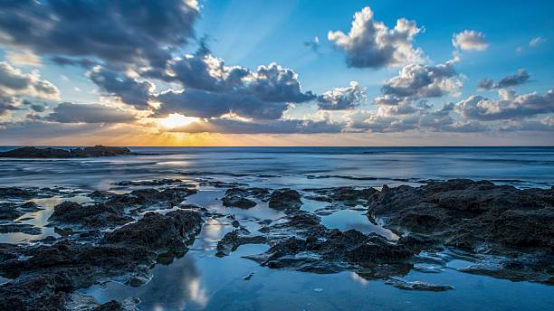 istock High resolution color panoramic long exposure landscape image of a beautiful sunset on the beach with natural rocks and cloud reflections in the water- Israel 2247577283