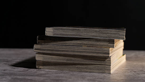 istock Stack of old paperback books on a textured surface, lit with soft shadows against a dark background, highlighting aged pages and a rustic reading atmosphere. 2247578142