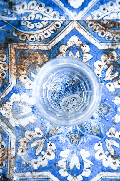 Glass of water on blue tile, sunlight casting soft reflections, ornate floral motif surrounding clear ripples, textured ceramic