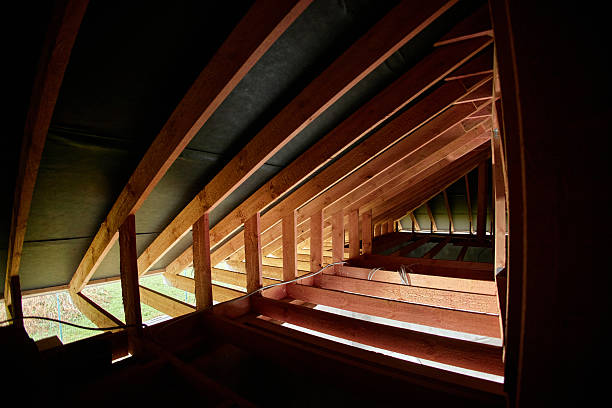 Wooden roof framework showing unfinished attic space with exposed beams and rafters, sunlight streaming through gaps, construction site highlighting structural details of building