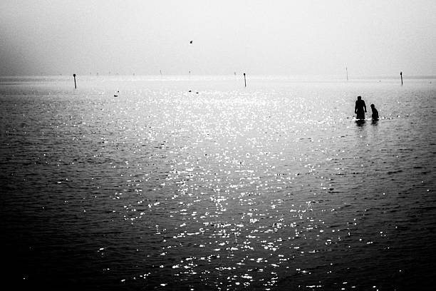 Silhouette of two people in waist-deep water under bright backlighting.
