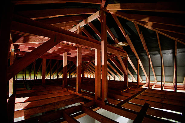 Wooden roof trusses forming structural framework of unfinished attic space, beams intersecting and supporting ceiling, sunlight filtering through gaps, construction in progress