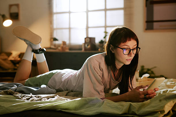 istock Young Biracial Woman Using Smartphone While Resting on Bed with Ankle Monitor 2247592632