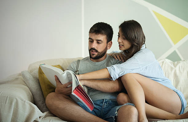Closeup front view of a young couple reading a magazine on a living room sofa.