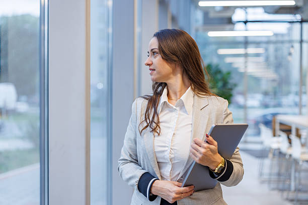 istock Businesswoman holding tablet looking away thinking in modern office 2247601512