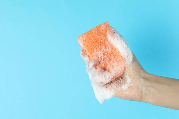 istock Woman holding sponge with foam on light blue background, closeup. Space for text 2247601756