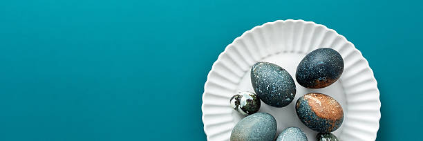istock A collection of intricately decorated Easter eggs in various shades rests on a white plate against a soothing teal backdrop, perfect for spring festivities and family traditions, banner 2247606331