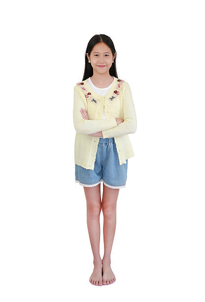 istock Full-length studio portrait young Asian girl smiling brightly while standing with her arms crossed. She is wearing light yellow cardigan with floral embroidery on white background. 2247609642