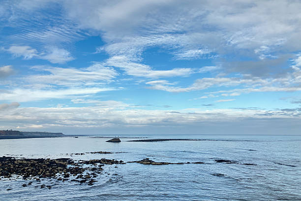 istock Rocks along the seashore with cloudy blue skies 2247611509