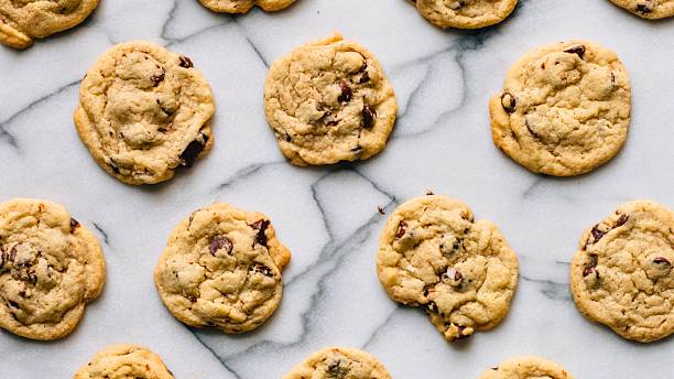 A top-down view of freshly baked chocolate chip cookies, showcasing their golden-brown texture and scattered chocolate chips on a white marble background.