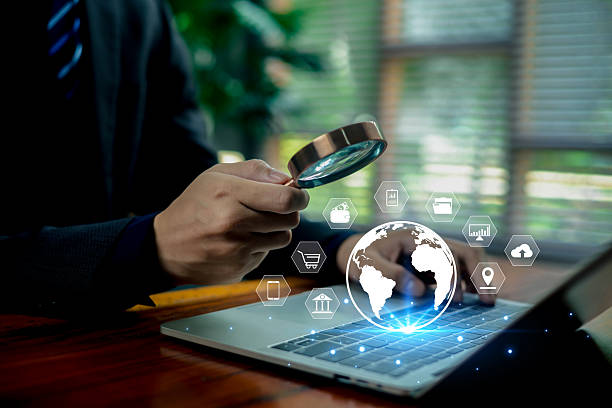 istock Business professional analyzing digital data with a magnifying glass over a laptop, surrounded by glowing global technology icons representing cybersecurity, analytics, and modern online services. 2247622451