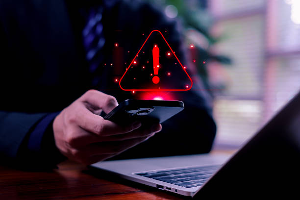 istock Business professional holding a smartphone with a glowing red warning alert icon, symbolizing cybersecurity threats, mobile security risks, and digital protection in modern technology environments. 2247623010
