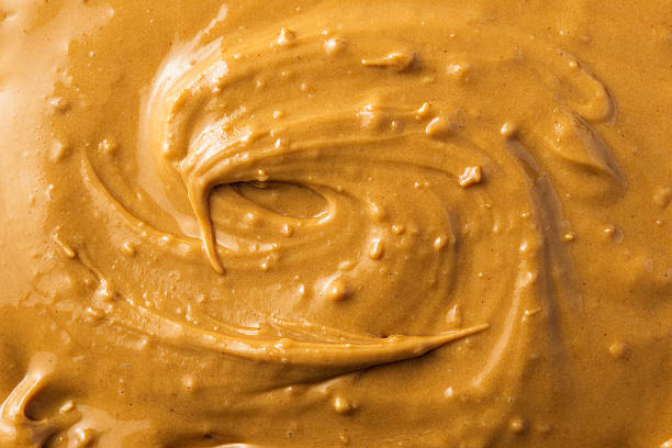 istock Creamy peanut butter texture in warm golden tones creates smooth appetizing background for sweets branding, bakery ads and food design. 2247628020