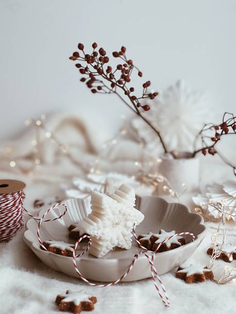 Elegant white snowflake-shaped candle Christmas decoration arranged in a plate with gingerbread cookies