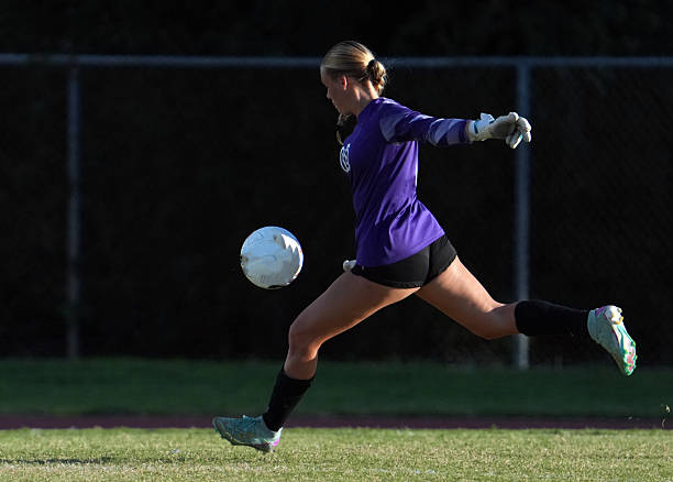 Female Soccer Goalie in uniform with cleats and gloves on a natural grass field in front of the goal/