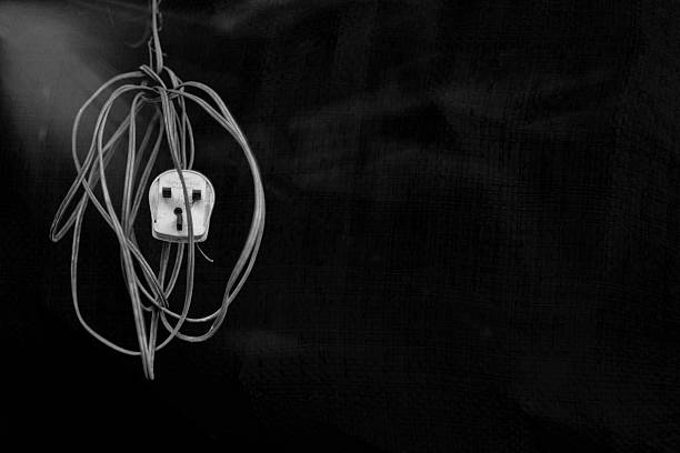 Monochromatic, low-key image of a tangled electrical plug resembling a skull, suspended in darkness with dramatic lighting.