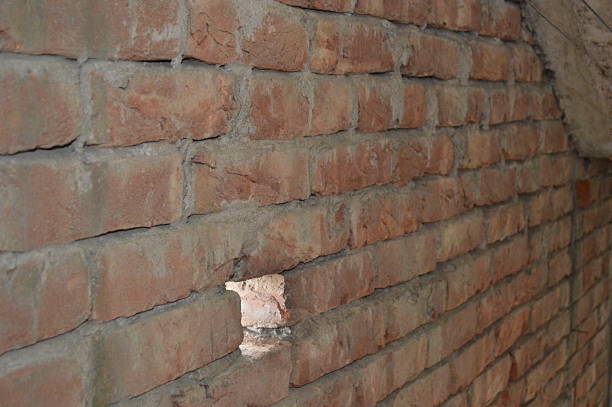 A raw brick interior with concrete beams and small daylight openings, capturing an industrial, unfinished construction scene and rugged textures of brick and concrete.