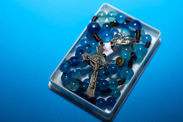istock ​A rosary with bright blue natural stone beads and a silver crucifix rests in a small rectangular white box on a saturated blue background. 2247641922