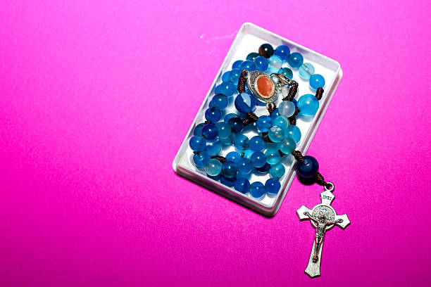 ​A rosary with a silver crucifix and vibrant blue natural stone beads, partially resting in a small white box on a bright pink (fuchsia) background.