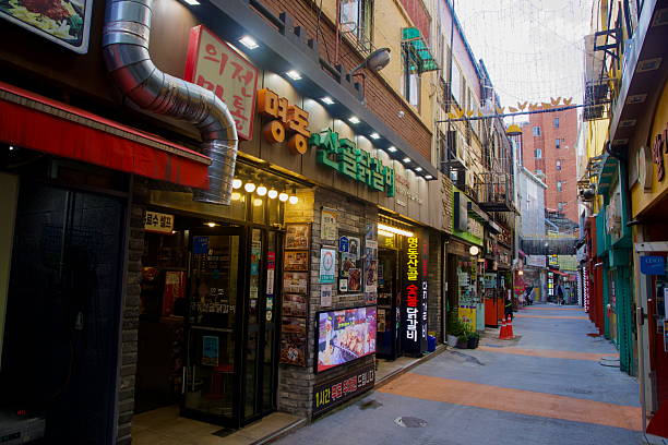 In Chuncheon City, South Korea, a row of dakgalbi restaurants facing a narrow pedestrian lane with string lights and colorful façades shows Chuncheon's commercial core on a clear day.