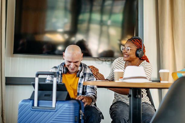 istock Multiracial couple waiting for transportation at cafe going on vacation with suitcases and looking at digital tablet 2247643436