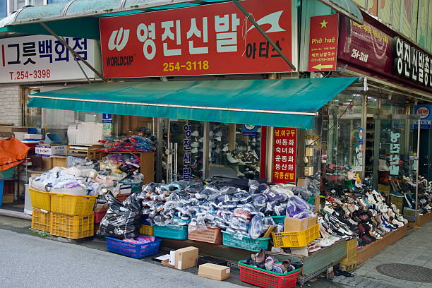 A shoe store at Chuncheon Central Market displays piles of packaged footwear and rows of sneakers spilling onto the sidewalk beneath bright awnings and Korean shop signs in the old downtown.