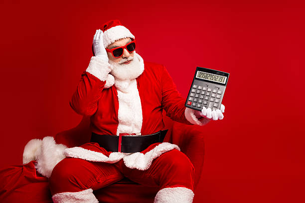 istock Santa in a red suit with sunglass holds a calculator against a bright red background for Christmas shopping and holiday fun 2247647787