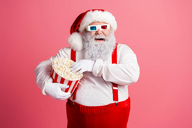 istock Santa with popcorn and three dimensional glasses in a pink studio enjoying a festive moment 2247647788