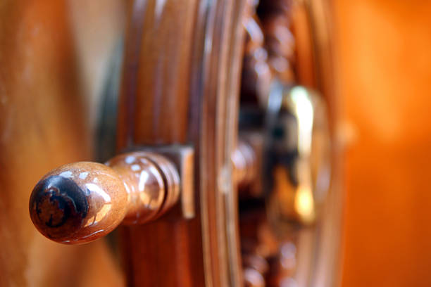 Detail of polished wooden boat helm with shallow depth of field and orange bokeh, symbolizing navigation, direction, leadership and marine travel.