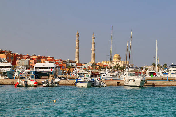 Scenic view of boats moored in Hurghada marina with mosque domes and minarets on Red Sea coast of Egypt under clear blue sky, popular holiday destination.