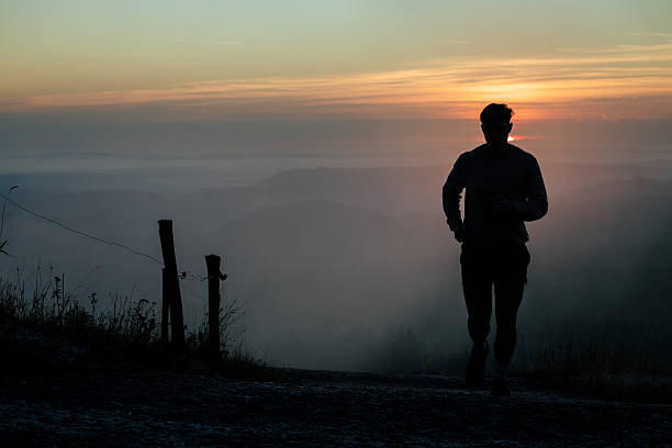Young man runs along hill top at sunrise, fog and mountain ranges below, Black Forest, Baden-Württemberg
