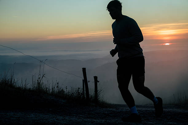 Young man runs along hill top at sunrise, fog and mountain ranges below, Black Forest, Baden-Württemberg