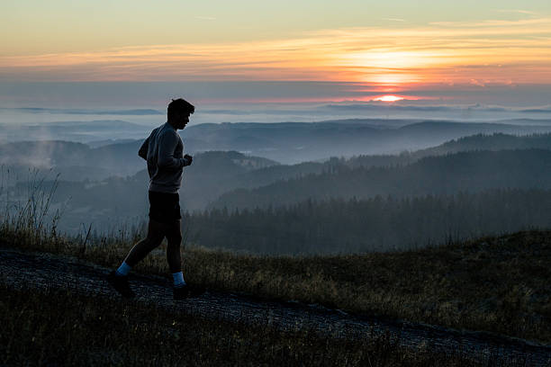 Young man runs along hill top at sunrise, fog and mountain ranges below, Black Forest, Baden-Württemberg