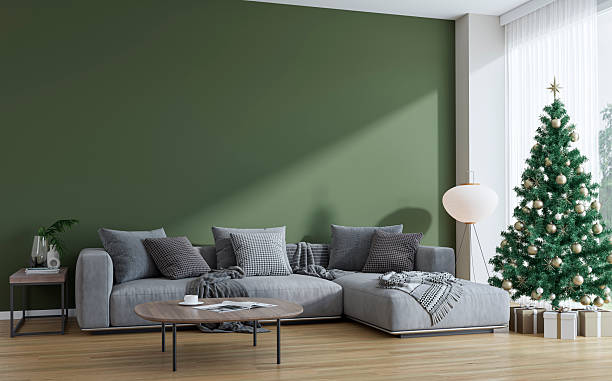 istock Modern living room decorated for Christmas, with a large gray sofa, table in front of a hunter green blank wall, Christmas tree in front of large windows with view 2247650184