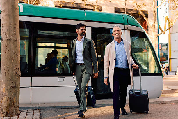 istock Businessmen traveling together pulling luggage by a tram 2247652682