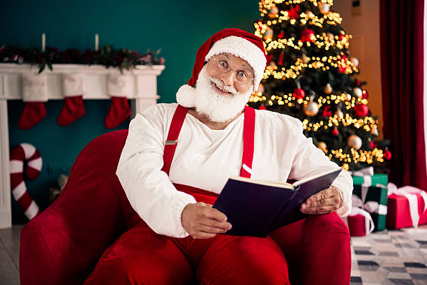 istock Santa reads a book while relaxing in a cheerful home Christmas scene with a lit tree and wrapped gifts 2247653866