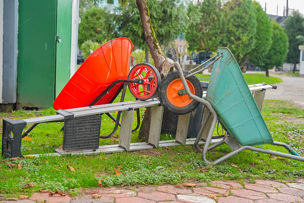 An empty wheelbarrow, garden cart in an autumn garden, against a background of trees and a lot of fallen dry yellow leaves with copy space. Seasonal gardening, plant care, gardening and farm tools.