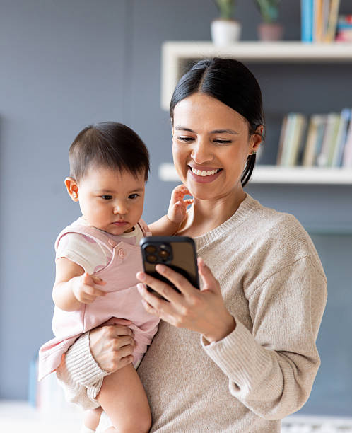 istock Loving mother texting on her phone while carrying a baby at home 2247662439